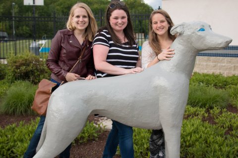 Assumption alumni posing by a statue of the University mascot, Pierre.